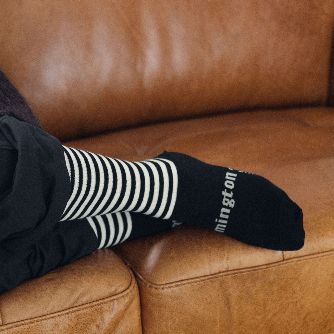 Merino Wool Crew Socks for Woman, featuring black and latte horizontal stripes, resting on a brown leather couch.