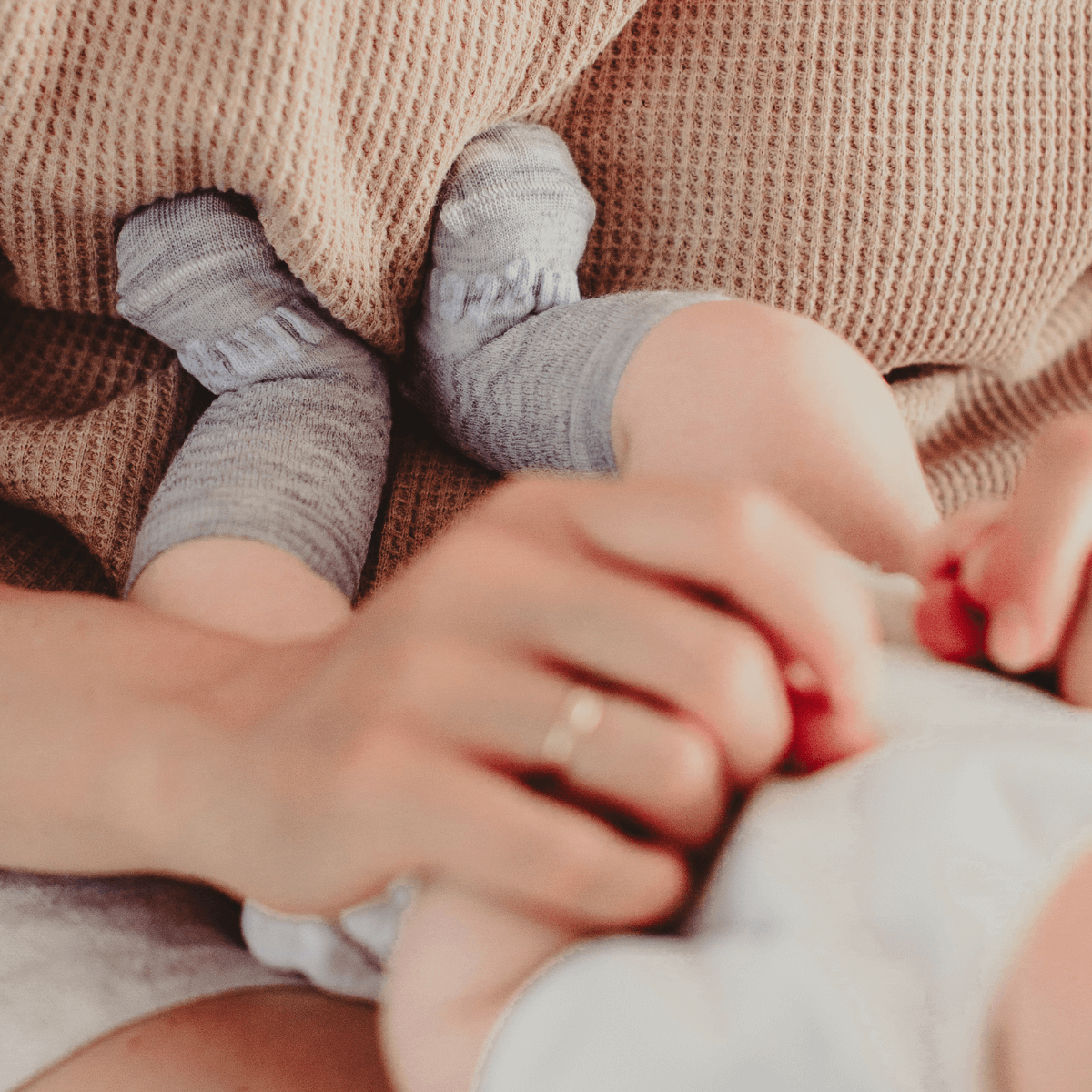 Baby wearing Merino Wool Crew Socks in light grey while a parent holds them.